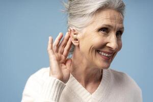 Smiling, happy senior gray haired woman having hearing aid in ear, isolated on blue background photo