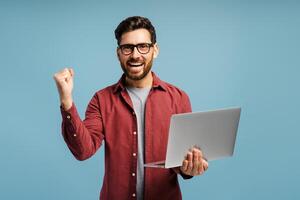 Smiling excited middle aged, Latin man, programmer holding laptop, using computer, win money photo