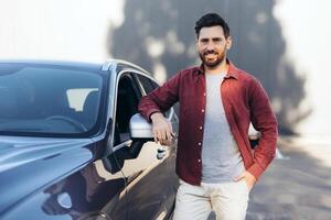 Confident, smiling Latin man, happy owner new car, looking at camera, standing outdoors. Transportation concept photo