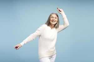 Happy, smiling senior woman with closed eyes, dancing, having fun, isolated on blue background photo