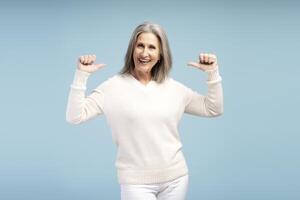 Smiling senior woman pointing fingers herself, posing isolated on blue background photo