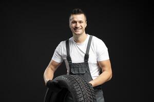 Mechanic holding winter tire smiling on black background photo