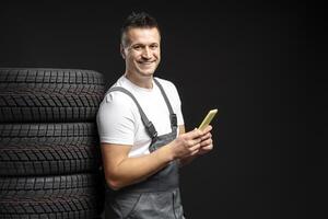 Mechanic using mobile phone next to stack of tires photo