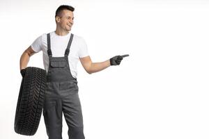 Mechanic holding tire and pointing with finger on white background photo