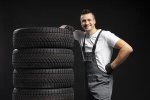 Mechanic leaning on stack of new winter tires posing on black background photo