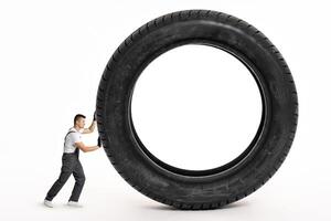 Mechanic pushing huge tire on white background photo