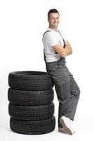 Mechanic leaning on stack of car tires with arms crossed smiling at camera photo