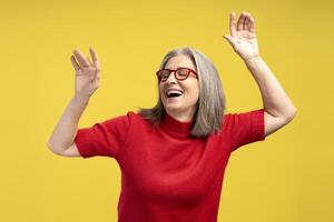Portrait of smiling, happy, senior woman wearing stylish eyeglasses, hands up, dancing photo