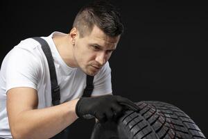 Mechanic inspecting winter car tire tread depth on black background photo