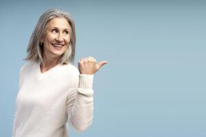 Happy, smiling, senior woman looking away, pointing finger on copy space showing mature female model photo