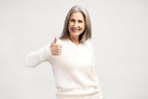 Smiling, positive gray haired woman showing ok gesture thumb up, posing isolated on white background photo