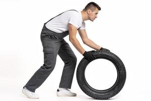 Mechanic pushing large tire on white background photo