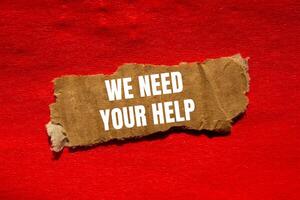 We need your help message written on ripped torn cardbaord paper piece with red background. Conceptual we need your help symbol. Copy space. photo