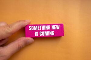 Something new is coming message written on pink wooden block with orange background. Conceptual something new is coming symbol. Copy space. photo