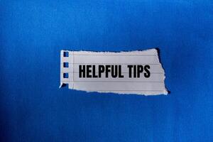 Helpful tips message written on ripped torn paper piece with blue background. Conceptual helpful tips symbol. Copy space. photo