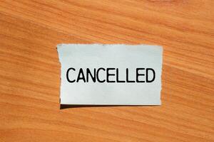 Cancelled message written on ripped torn paper piece with wooden background. Conceptual cancelled symbol. Copy space. photo