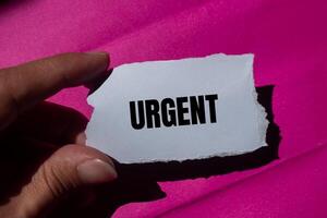 Urgent message written on ripped torn paper piece with a pink background. Conceptual urgent word symbol. Copy space. photo
