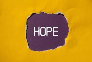 Hope message written on ripped torn yellow paper with purple background. Conceptual hope symbol. Copy space. photo