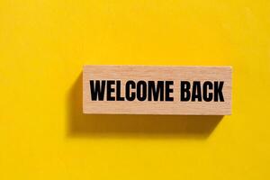 Welcome back message written on wooden block with yellow background. Conceptual welcome back symbol. Copy space. photo
