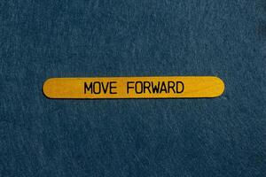Move forward message written on yellow wooden stick with gray background. Conceptual move forward symbol. Copy space. photo