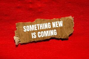 Something new is coming message written on ripped torn cardbaord paper piece with red background. Conceptual something new is coming symbol. Copy space. photo