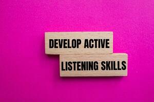 Develop active listening skills message written on wooden blocks with pink background. Conceptual develop active listening skills symbol. Copy space. photo
