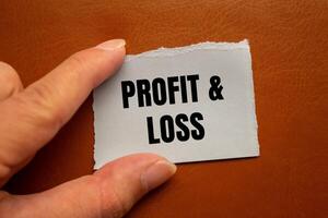 Profit and loss message written on ripped torn paper piece with brown background. Conceptual profit and loss symbol. Copy space. photo