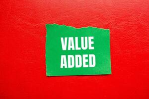Value added message written on ripped torn green paper piece with red background. Conceptual value added symbol. Copy space. photo