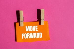 Move forward message written on ripped torn orange paper piece with pink background. Conceptual move forward symbol. Copy space. photo