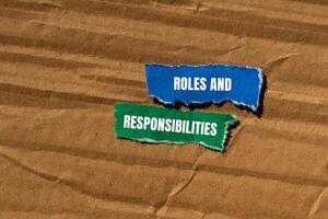 Roles and responsibilities message written on ripped torn paper pieces with cardboard background. Conceptual roles and responsibilities symbol. Copy space. photo