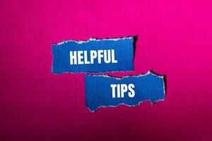 Helpful tips message written on ripped torn blue paper pieces with pink background. Conceptual helpful tips symbol. Copy space. photo
