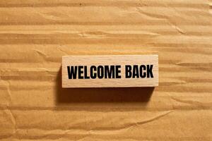 Welcome back message written on wooden block with cardboard background. Conceptual welcome back symbol. Copy space. photo