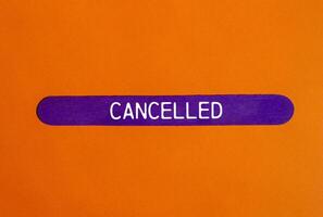 Cancelled message written on purple wooden stick with orange background. Conceptual cancelled symbol. Copy space. photo