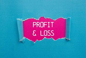 Profit and loss message written on ripped torn blue paper with pink background. Conceptual profit and loss symbol. Copy space. photo