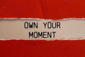 Own your moment message written on ripped torn red paper with beige background. Conceptual own your moment symbol. Copy space. photo