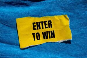 Enter to win message written on ripped torn yellow paper piece with blue background. Conceptual enter to win symbol. Copy space. photo