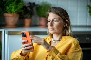 Thoughtful relaxed European woman looking to screen cellphone reading message, scrolling web at home photo
