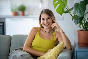 retrato contento relajado mujer a hogar descanso a acogedor sofá sonriente mirando a cámara. planta amante hogar. foto