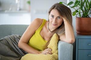Relaxed woman sitting on sofa spending lazy time at home look at camera with calm emotion. Slow life photo