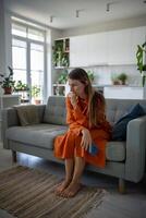 Depressed woman sits on couch reflecting deep in thought with phone in hand thinking about problems photo