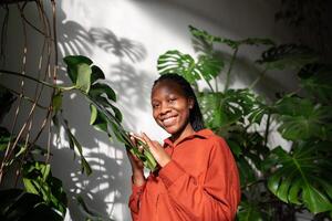 retrato, alegre africano americano mujer entre urbano selva. planta amante niña a soleado invernadero foto