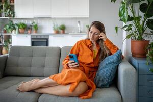 calma enfocado mujer utilizar Teléfono móvil sentado en sofá haciendo en línea compras o orden entrega. foto