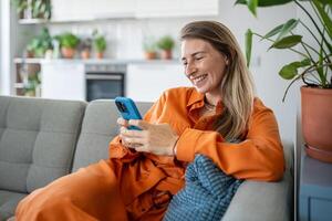 contento sueco mujer utilizando teléfono inteligente, descansando a sofá a acogedor hogar y desplazamiento social redes foto