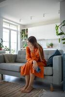 Unhappy sad woman in difficult situation sitting at home on couch with smartphone received bad news photo