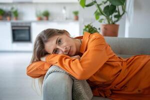 Portrait of relaxed woman lying on sofa with head bowed on armrest look at camera with calm emotion. photo