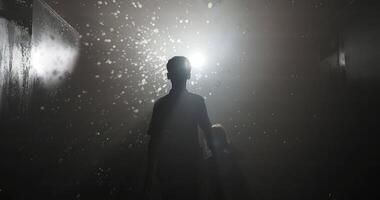 Silhouetted view of two children, one larger and one smaller, playing with soap bubbles in a misty room, reaching out with fingers to pop the bubbles against a bright light video