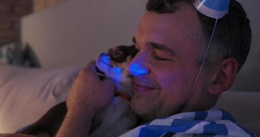 Man in pajamas and a birthday hat cuddles his chihuahua, creating a cozy and affectionate atmosphere at home video