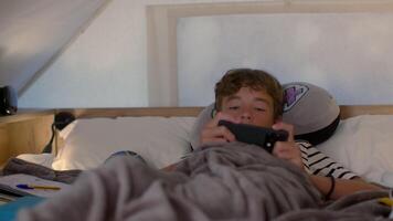 Teen boy lying in bed inside a glamping tent, using a smartphone. The setting is cozy and comfortable, with soft bedding and various personal items nearby video