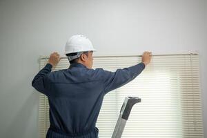 Back View of Worker Installing Window Blinds with Safety Gear in Residential Room photo