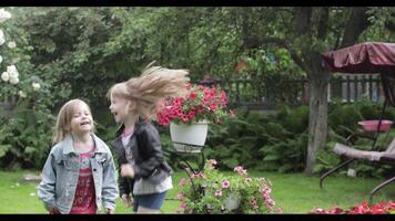 Children have fun in the rain. Two sisters are running around having fun in the rain in the yard at home. video
